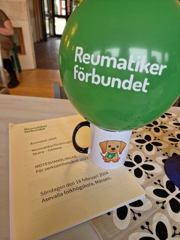 På ett bord ligger årsmöteshandlingarna, Reumatikerförbundets mugg, och i den den gröna ballongen